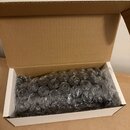 Otevřená hnědá kartonová krabice, ve které se nachází předměty zabalené do průhledné bublinkové fólie. Vnitřek krabice je bílý. Na předmětech nejsou…