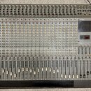 Široký míchací pult s šedým povrchem a černým rámem. Na pravé straně je červené logo TASCAM a vedle něj vertikální nápis M-2524. Přístroj obsahuje ve…
