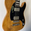 Elektrická kytara s přírodním dřevěným povrchem těla a černým pickguardem. Nástroj má dva humbuckery, chromovaný most a jeden ovládací knoflík. Na hř…
