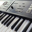 Černý digitální klavír s bílými a černými klávesami. Na ovládacím panelu jsou viditelné nápisy ARPEGGIO/RHYTHM, SEQUENCER a SAMPLER, množství bílých…