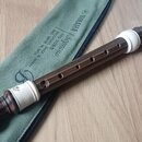 Hnědá sopránová bloková flétna s bílými plastovými spojkami a koncovkou. Na těle nástroje je vidět logo Yamaha. Flétna leží na zeleném plátěném pouzd…