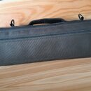 Černý textilní obal na hudební nástroj s rukojetí a dvěma úchytky pro popruh. Na pravé straně je přišitý štítek s logem a nápisem SANKYO Flutes. Obal…