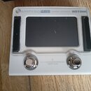 Bílý efektový procesor s černým displejem. V horní části je nápis AMPERO MINI Amp Modeler / Effects Processor a logo HOTONE. Dole jsou dvě kovové kon…