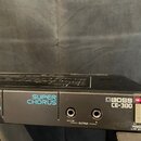 Černý rackový efekt s nápisy SUPER CHORUS a BOSS CE-300. Na předním panelu jsou dva výstupní konektory označené jako A(A+B) a B pod společným nápisem…