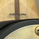 Detail zadní strany krku kytary z přírodního dřeva s tmavým středovým pruhem. Na dřevě je černý nápis MADE IN JAPAN a pod ním sériové číslo H022624.…