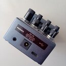 Stříbrný kovový efekt pedál s několika černými oválnými knoflíky. Na horní straně jsou konektory a nápisy PHONES, DC IN USE BOSS PSA ADAPTER ONLY 9V.…