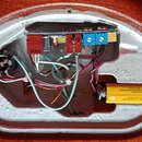 Fotografie zachicuje vnitřek elektroniky v nástroji s hnědým lakem. Je zde vidět červený a modrý potenciometr, zapojená kabeláž a žlutá 9V baterie. N…