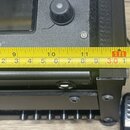 Detailní záběr na šedý elektronický přístroj s displejem a ovládacím knoflíkem. Na povrchu je viditelný nápis HOME. Před přístrojem je přiložen žlutý…