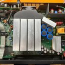 Fotografie zachycuje vnitřek elektronického zařízení s otevřeným šasi. Uprostřed dominuje velký hliníkový chladič s čtyřmi žebry, nad kterým je umíst…