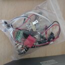 Průhledný plastový sáček s elektronickými součástmi pro hudební nástroj. Uvnitř jsou vidět potenciometry, červený konektor a růnobarevné vodiče (bílé…