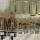 Fotografie zobrazuje skupinu elektronických vakuových trubic (lamp) a šest kovových krytů. Mezi lampami jsou viditelné nápisy TUNG-SOL MADE IN RUSSIA…