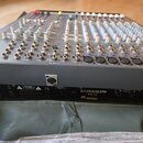 Šedý mixážní pult s bílými a barevnými ovratovými knoflíky. Na zadní straně je černý nápis ALLEN&HEATH PA12 a varovný štítek CAUTION. Jsou vidět různ…