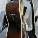 Detail hnědé akustické kytary s bílým lemováním. Na boku je umístěn ovládací panel s nápisy „TREBLE“, „BASS“ a „VOLUME“ a logem „Ibanez“. Pod logem j…