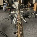 Detailní pohled na horní část saxofonu v kovovém provedení s viditelným opotřebením povrchu a patinou. Na hrdle je nasazen jamor. V pozadí jsou vidět…