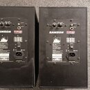 Dva černé studiové monitory značky SAMSON z řady Rubicon. Na zadní straně jsou viditelné ovládací prvky Volume a Ribbon Level, vstupy -10 INPUT a +4…