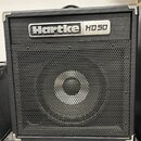 Černý basový kombo zesilovač s kovovou ochrannou hranou. V horní části je stříbrný nápis Hartke HD 50 a pod ním černá kovová mřížka reproduktoru. Zes…