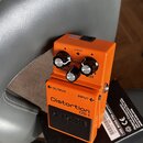 Oranžový kytarový efekt s nápisy Distortion DS-1 a BOSS. Na horní části jsou tři ovládací knoflíky s popisky LEVEL, TONE a DIST, dále nápis CHECK a s…