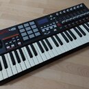 Černý MIDI kontrolér s klaviaturní součástí a bílými a černými klávesami. Na levé straně je nápis AKAI professional MPK49 a mřížka šedých padů. Horní…