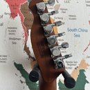 Záběr na hřif a hlavu kytary z tmavého dřeva s šesti chromovanými ladičkami. Na zadní straně hlavy je čitelný nápis: „MADE IN INDONESIA S.E.A. ROLLS…