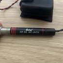 Černý cylindrický konektor s kovovou částí a červenými vodorovnými proužky. Na černém povrchu je bílý nápis Belcat AP-55 AP JACK. Konec konektoru je…