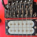 Detail červené elektrokytary s černým kladeným mostem a humbuckerem. Na mostu je nápis Licensed Under Floyd Rose Patents, v oblasti sedla jsou vidite…