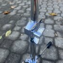 Detail chromovaného kovového stojanu s utahovacím šroubem a křídlovým knoflíkem. Povrch je lesklý, bez viditelných značek či nápisů. Stojan stojí na…