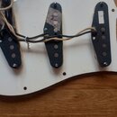 Fotografie zachicuje spodní stranu bílého pickguardu s třemi černými snímači typu single-coil. Střední snímač má na povrchu nalepenou pásku s fialový…