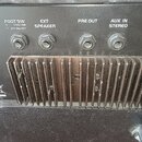 Detail zadní strany černého zesilovače s kovovým chladičem. Jsou zde čtyři konektory s nápisy FOOT SW (CHA/CHB, EFF ON/OFF), EXT SPEAKER, PRE OUT a A…