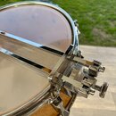 Detailní záběr na horní část bubnu s napnutou blánou. Na povrchu je umístěn kovový, chromovaný throw-off mechanismus s texturovaným povrchem. Nástroj…