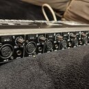 Černý rackový audio rozhraní s kovovým stříbrným rámem. Na levé straně je nápis ULTRAGAIN PRO-8 DIGITAL, 8 CHANNEL A/D & D/A CONVERTER MODEL ADA8000.…