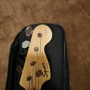 Fotografie zachycuje hlavu basové kytary v černé softcase kabelce. Na dřevěné hlavě je černý nápis Squier by Fender® P-BASS®. V horní části je drobný…