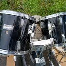 Dvě černé bubny z bicí sady značky TAMA, model SWINGSTAR. Na obou jsou viditelné štítky s nápisy „SWINGSTAR by TAMA“ a „MADE IN TAIWAN“. Povrch je če…