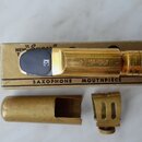 Zlatý mosazný saxofonový mouthpiece s černým náústkem, položený na kartónové krabičce. Na mouthpiece je vyryt nápis "Otto Link". Krabička obsahuje te…