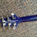 Zadní strana hlavy modré elektro kytary s chromovanými ladičkami. Na zadní straně hlavy je bílý nápis: Built by Cor-Tek Musical Instrument Co., LTD,…