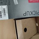Fotografie zachicuje část šedé krabice s nápisem PICKUP a logem EMG. Na krabici je nalepená bílá štítková nálepka s textem EMG-57 PICKUP, BLACK CHROM…