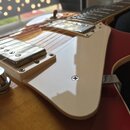 Detail elektrické kytary s červeným a žlutým lakem. Nástroj má dva chromované humbuckery v bílých rámečcích a bílý plechtrát. Na kytaru nejsou vidite…