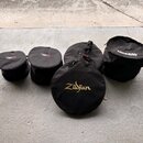 Pět černých textilních přepravních tašek na činely v různých velikostech. Na jedné z tašek je zlatý nápis Zildjian, na jiné bílý nápis ROCKBAG a na d…