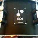 Detail černého bubnu s chromovaným kováním. Uprostřed je čtvercový černý štítek s bílým nápisem SQ1, MADE IN GERMANY a logem SONOR. Povrch nástroje j…