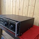 Černý rackový výkonový zesilovač s kovovým šasi a dvěma ovládacími knoflíky. Na předním panelu je bílý nápis SEAK PA 410 POWER AMPLIFIER. Povrch šasi…