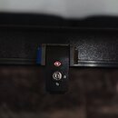 Detailní záběr na černý zámek s kroužkem pro klíč, který je součástí kufru. Na horní části zámku je červený kosočtvercový symbol s bílým znakem uvnit…