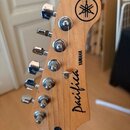 Detail hlavy dřevěné kytary s šesti chromovanými ladičkami. Na dřevě je vidět kulaté logo YAMAHA a nápisy YAMAHA a Pacifica. Povrch dřeva je světlý a…