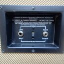 Detail zadní strany reproduktorové skříně s černým kovovým rámem. Jsou zde dva konektory jack, popisky LEFT INPUT a RIGHT OUTPUT, přepínač STEREO/MON…