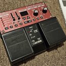 Červený loop pedal s černými pedály, na kterém je nápis RC-30 DUAL TRACK LOOPER a logo BOSS. Zařízení obsahuje různé přepínače, potenciometry a ovlád…