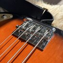 Detail chromovaného mostu na kytaru s oranžovým povrchem. Na horní části mostu je viditelný nápis GOTOH JAPAN. Most obsahuje pět strun s viditelnými…