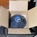 V otevřeném kartónovém boxu je umístěn reproduktor s šedým kovovým rámem a modrým středovým štítkem. Na štítku je bílý nápis JENSEN a pod ním označen…