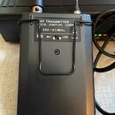 Černý obdélníkový vysílač s kovovým drátem v podobě klipu na povrchu. Na horním štítku je nápis HF TRANSMITTER, FCC ID.: JEBUT-18C (CE0336) a rozsah…
