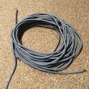 Šedý kabel svynutý do kroužku, položený na béžovém koberci. Konce kabelu jsou odizolovány a vidět jsou na nich měděná jádra. Na povrchu kabelu nejsou…