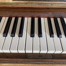 Detail klaviatury pianina s bílými a černými klávesami. Nástroj je zasazen do dřevěného rámu s viditelnými známkami opotřebení a škrábancemi na laku.…