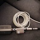 Stříbrný mikrofon s kovovou mřížkou a připojeným bílým kabelem. Na těle mikrofonu je viditelný nápis: „AKG“, „MADE IN AUSTRIA“, „VIENNA“. Povrch vyka…