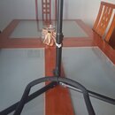 Černý kovový stativ s trojnožkou, který stojí na stole. Na středovém sloupku je viditelný bílý nápis „agg“. Povrch stativu vykazuje mírné známky opot…